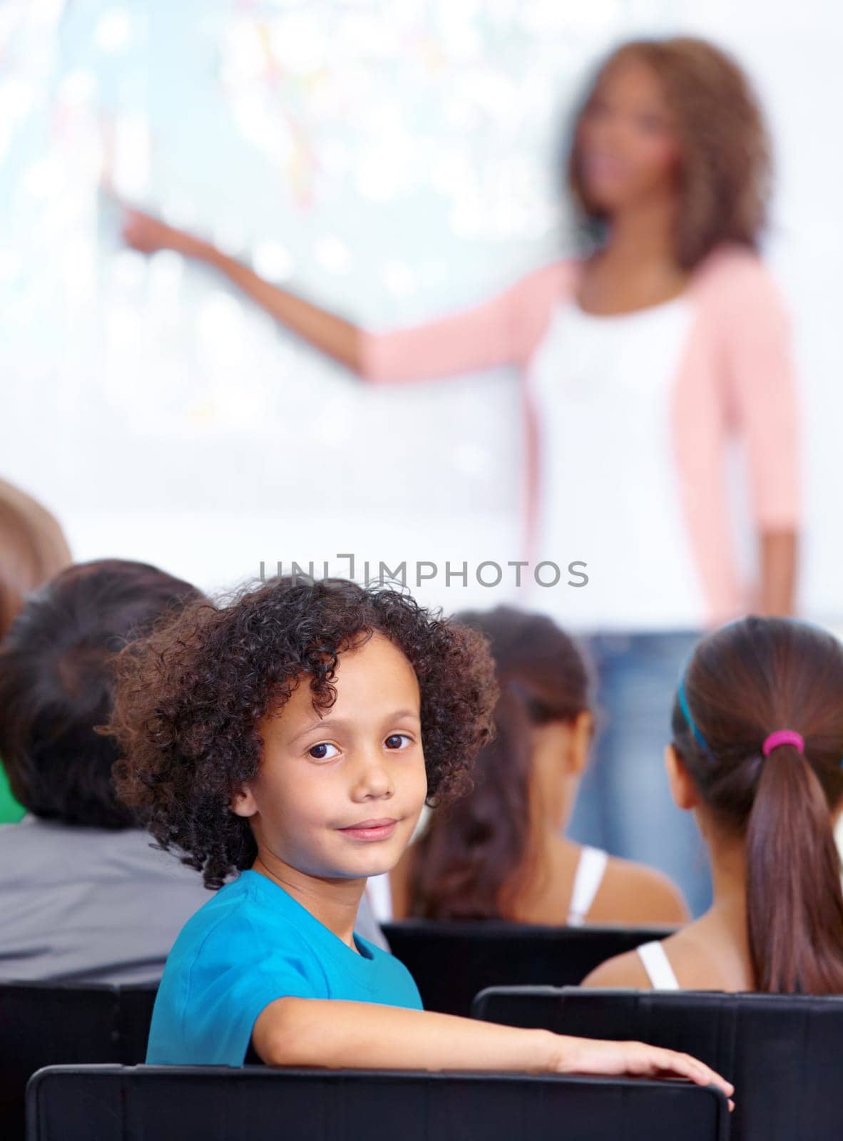 Portrait, boy child or student in classroom for knowledge, education or development for future growth. School, teacher blur or back of a clever kid with book or pride for studying or learning at desk.