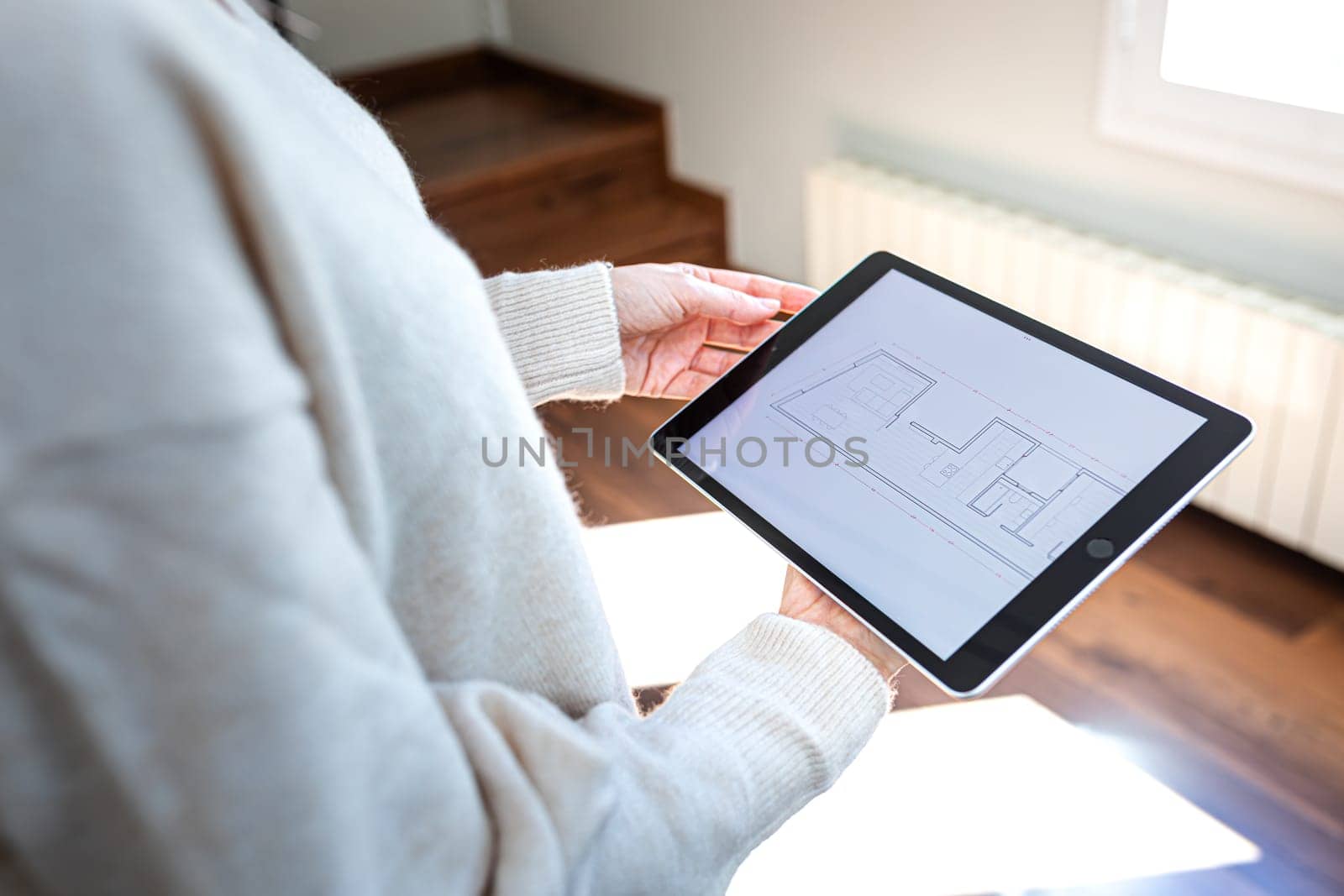 POV of woman holding digital tablet looking at floor plan standing indoors. by Hoverstock