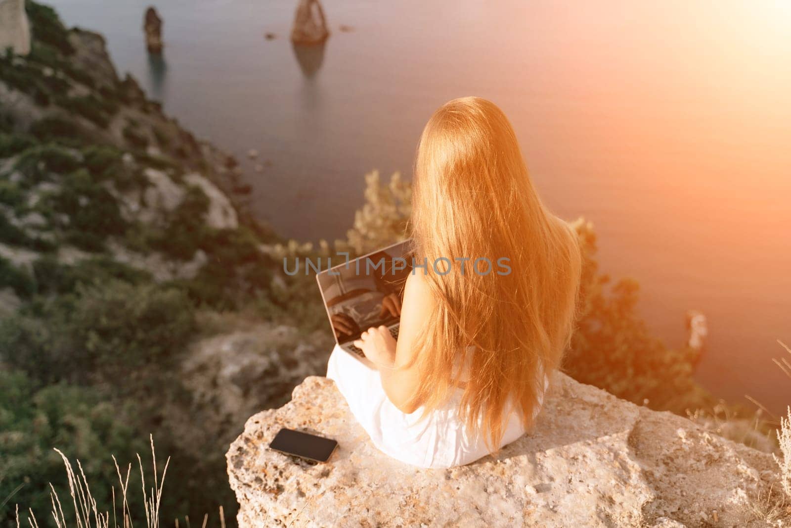 Freelance happy woman typing on her laptop, enjoying the picturesque sea view, highlighting the idea of working remotely with a relaxed and pleasant atmosphere