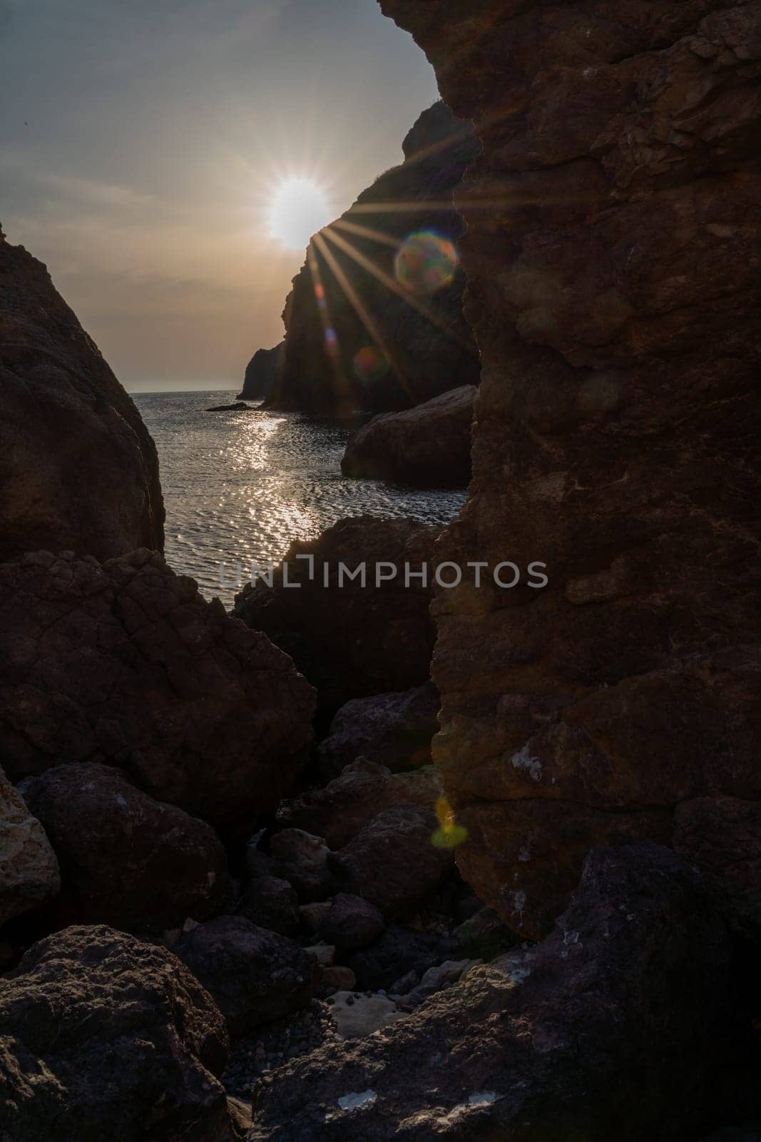 Woman tourist enjoying the sunset over the sea mountain landscape. Sits outdoors on a rock above the sea. She is wearing jeans and a blue hoodie. Healthy lifestyle, harmony and meditation by Matiunina