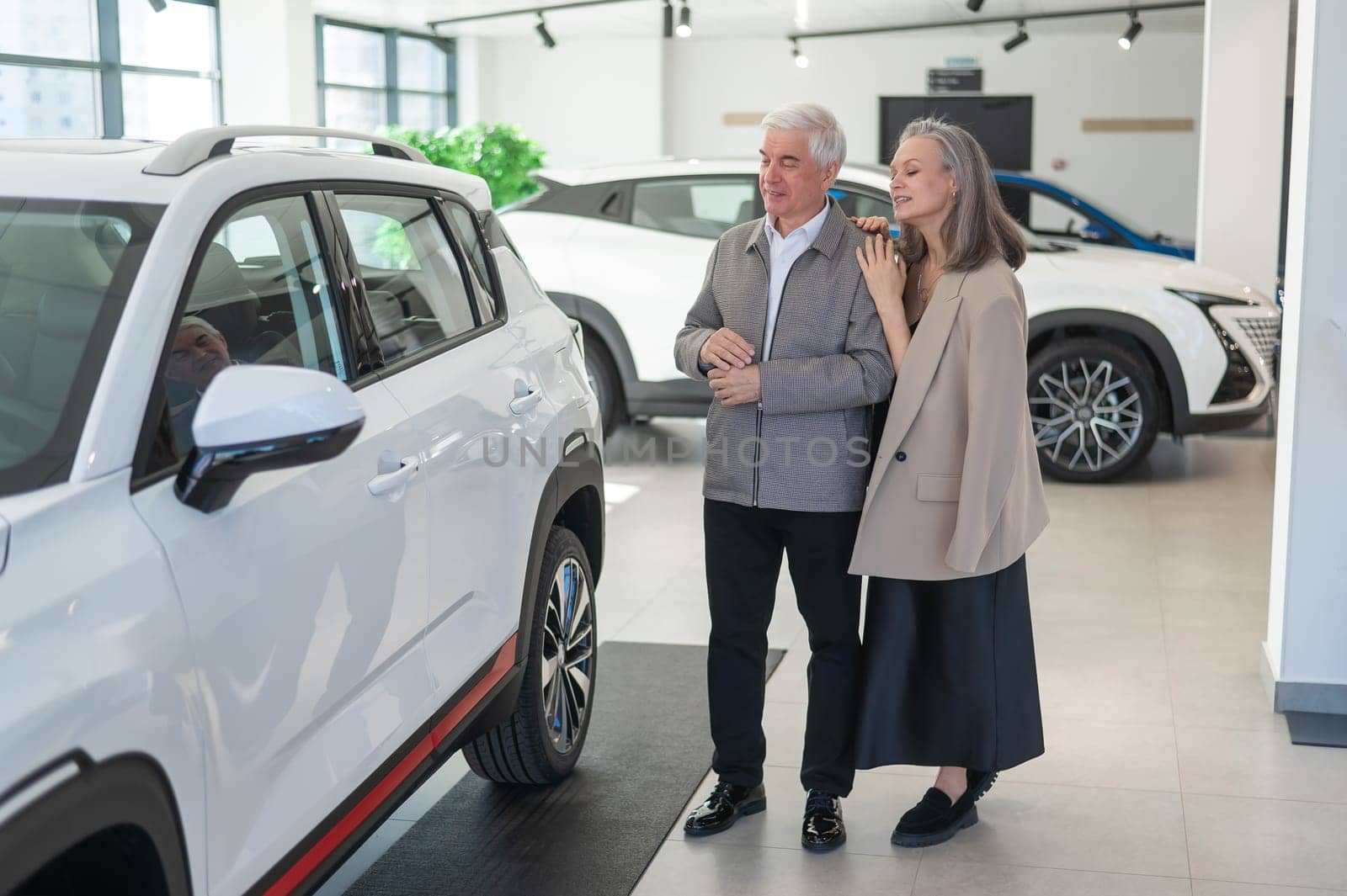 An elderly Caucasian couple chooses a new car at a car dealership. by mrwed54