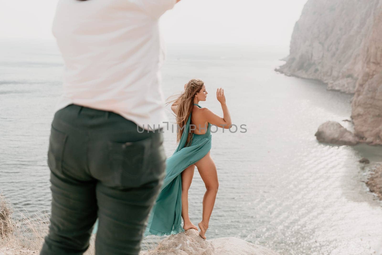 Woman travel portrait. Happy woman with long hair looking at camera and smiling. Close up portrait cute woman in a mint long dress posing on a volcanic rock high above the sea by panophotograph