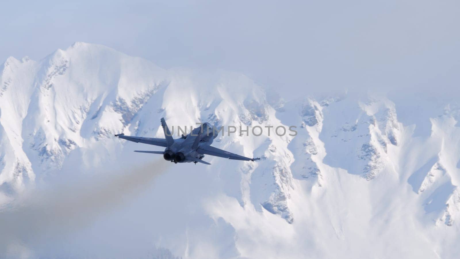 Meiringen Switzerland January 19 2023: Silhouette of fighter jet plane in flight. Snow capped mountains background on a sunny winter day. Copy Space. Boeing F-18 Hornet of Swiss Air Force WEF security