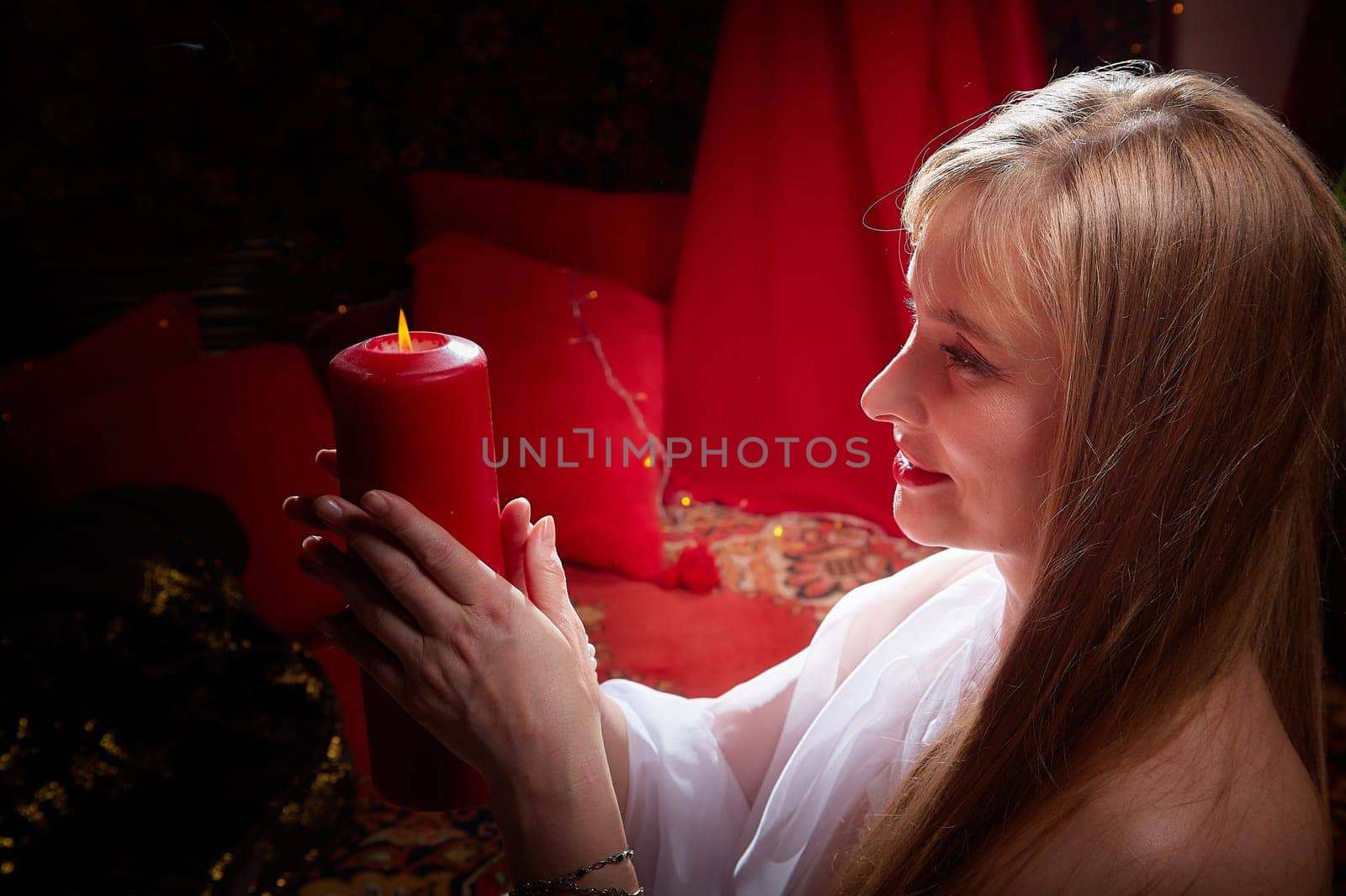 Beautiful arabian girl with candles in red room full of rich fabrics and carpets in sultan harem. Photo shoot of woman an oriental style odalisque. Model poses in sari as a caring wife and hostess by keleny