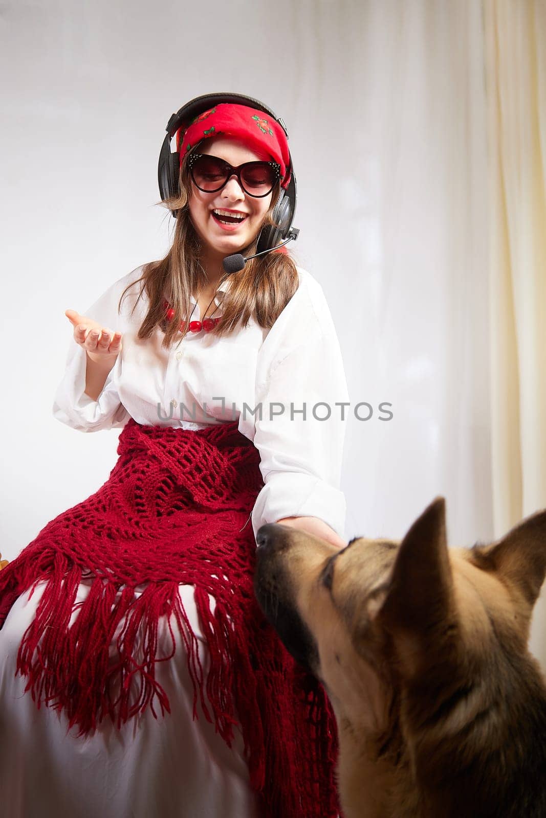 Young girl in red scarf, large headphones with microphone and black glasses and big shepherd dog. Woman who is radio or television presenter, female telecom operator, blogger, Freelancer and animal by keleny