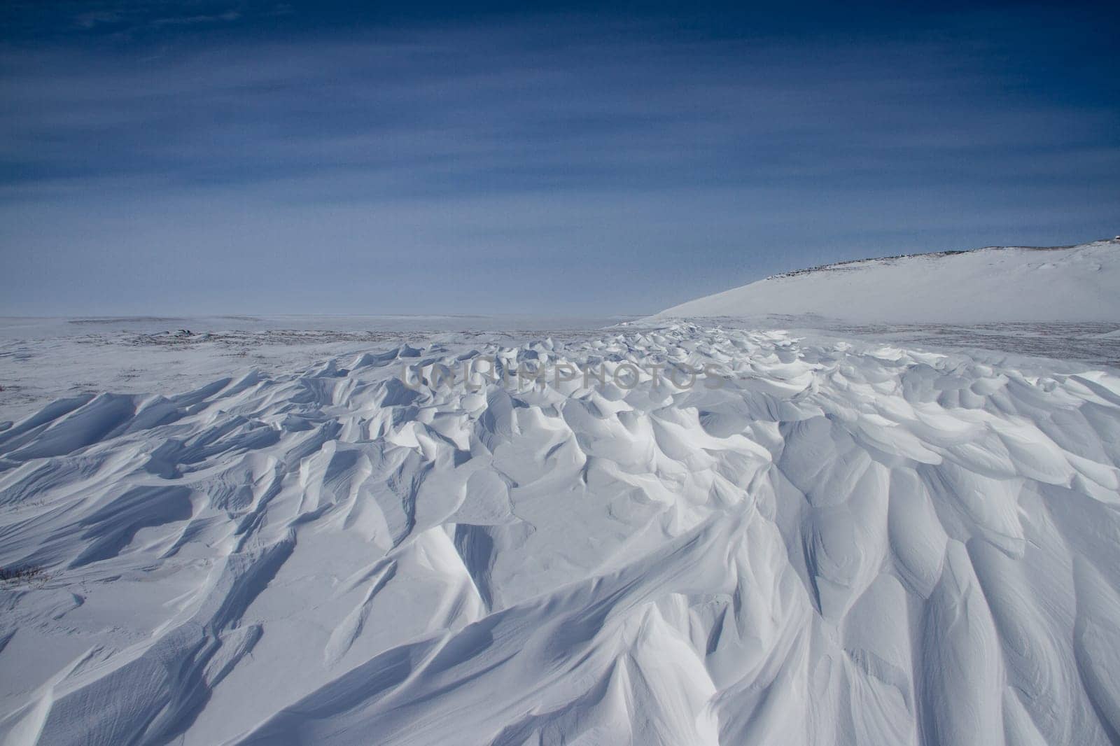 Beautiful patterns of sastrugi, parallel wavelike ridges caused by winds on surface of hard snow, with soft clouds in the sky, near Arviat Nunavut Canada