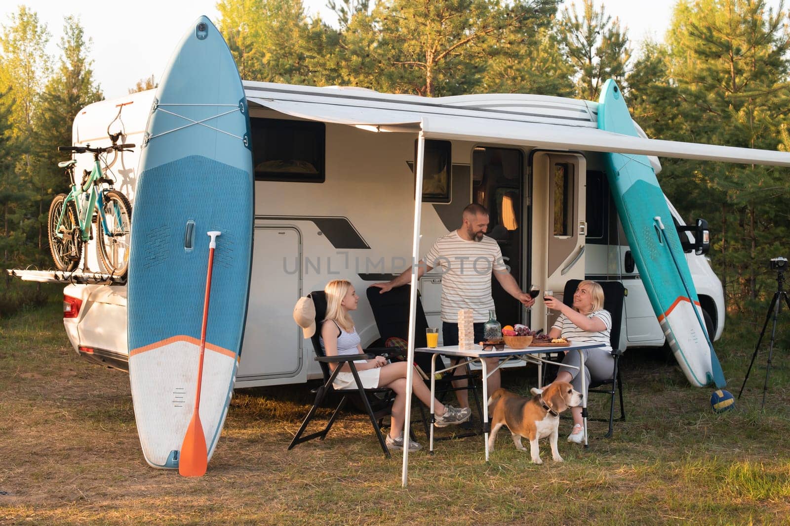 A happy family is resting nearby near their motorhome in the forest.