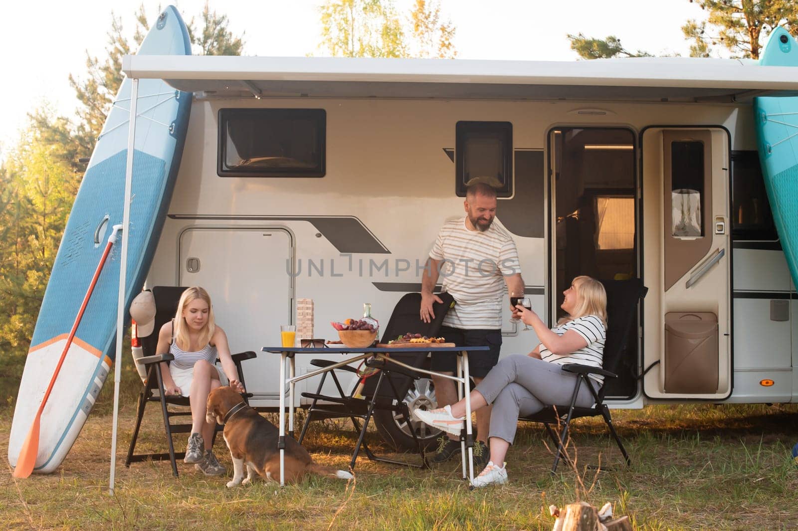 A happy family is resting nearby near their motorhome in the forest.
