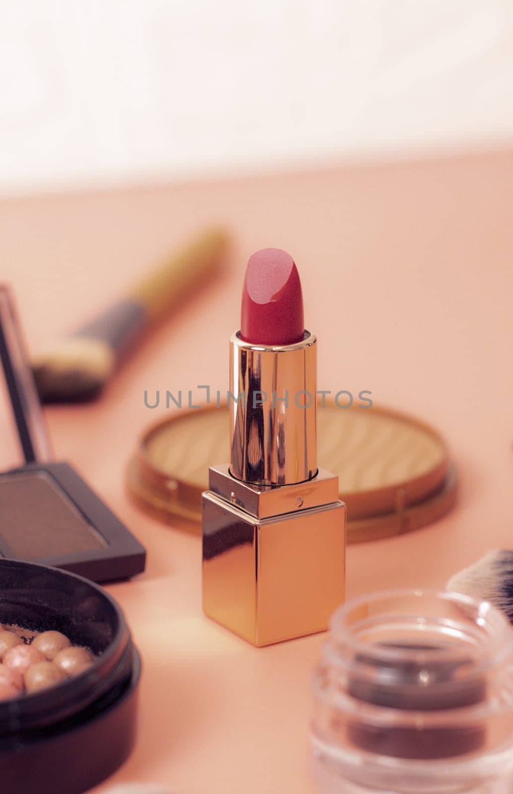 Red lipstick on a peach background with a set of cosmetics, close-up side view. The concept of cosmetics, beauty salon.