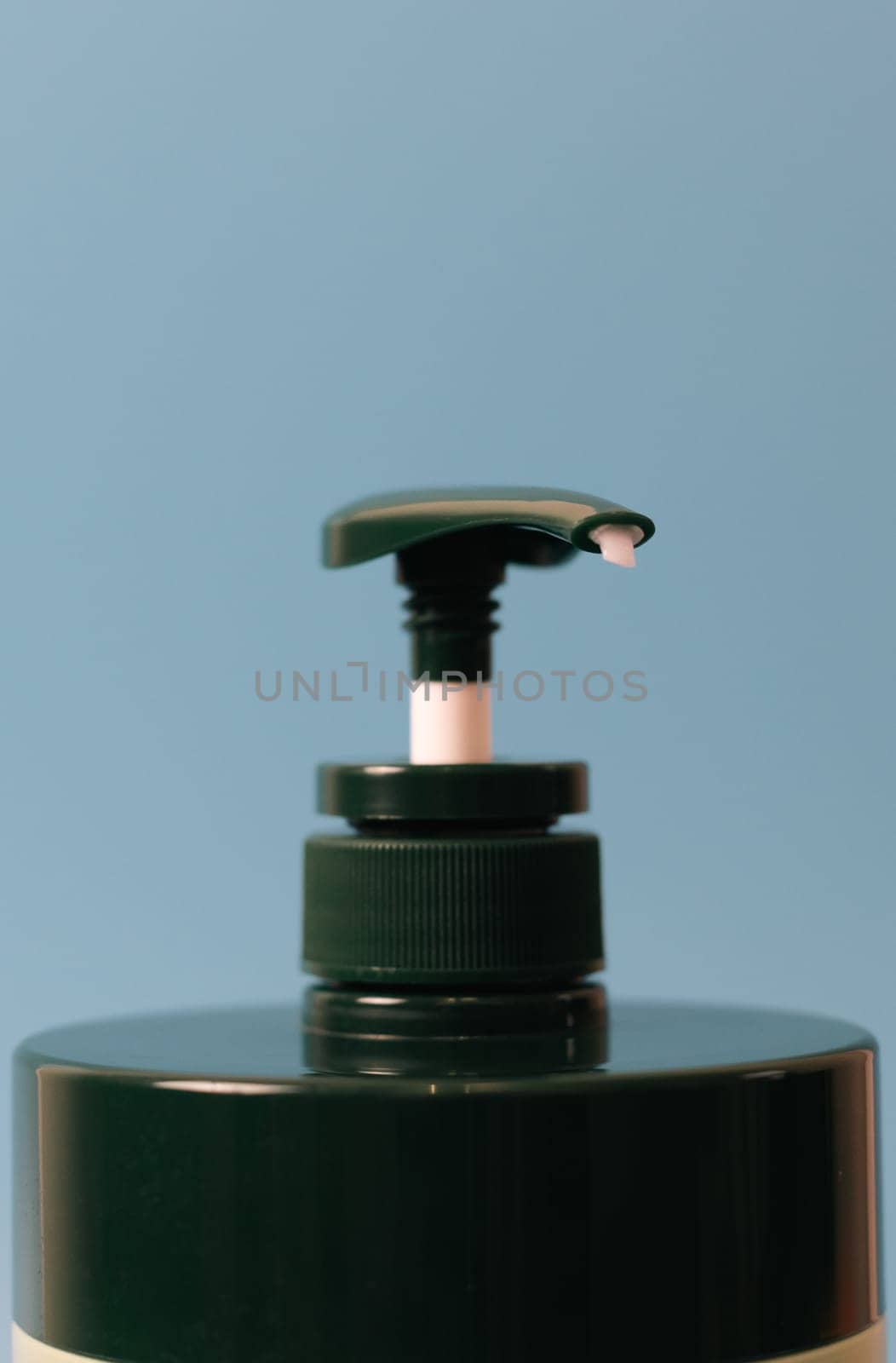 One bottle of green natural shampoo with a dispenser on a blue background, close-up side view. The concept of personal hygiene, cosmetics, beauty.