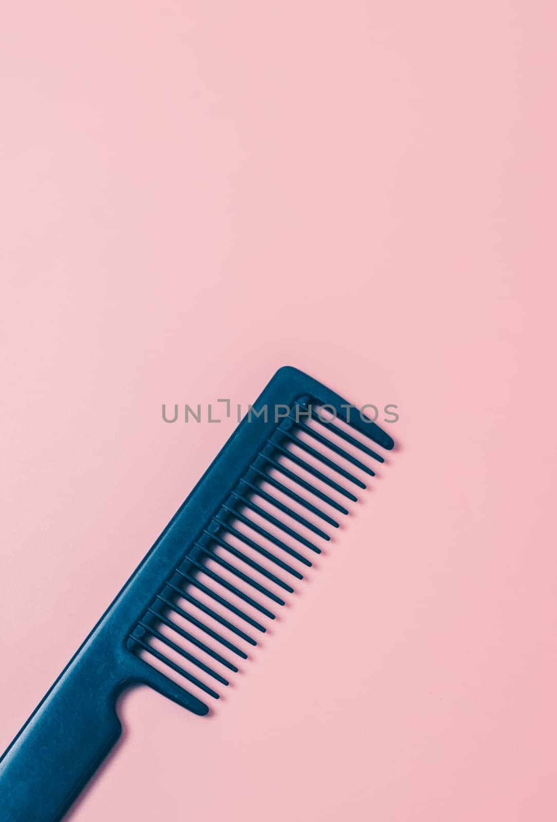 One black comb hairdresser on a pink background, flat lay close up. The concept of hairdressing, beauty salon, tools.