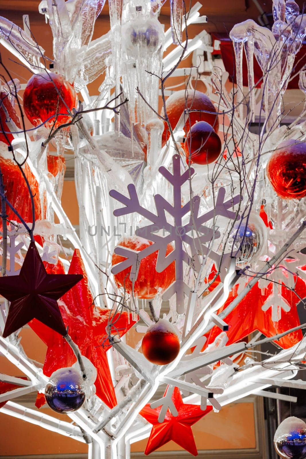 Close-up footage of Christmas Decorations on a Snow-Covered Spruce Tree in dusk, It's snowing, snowflakes are falling, red glass balls and stars, artificial snowflakes, illumination by vladimirdrozdin