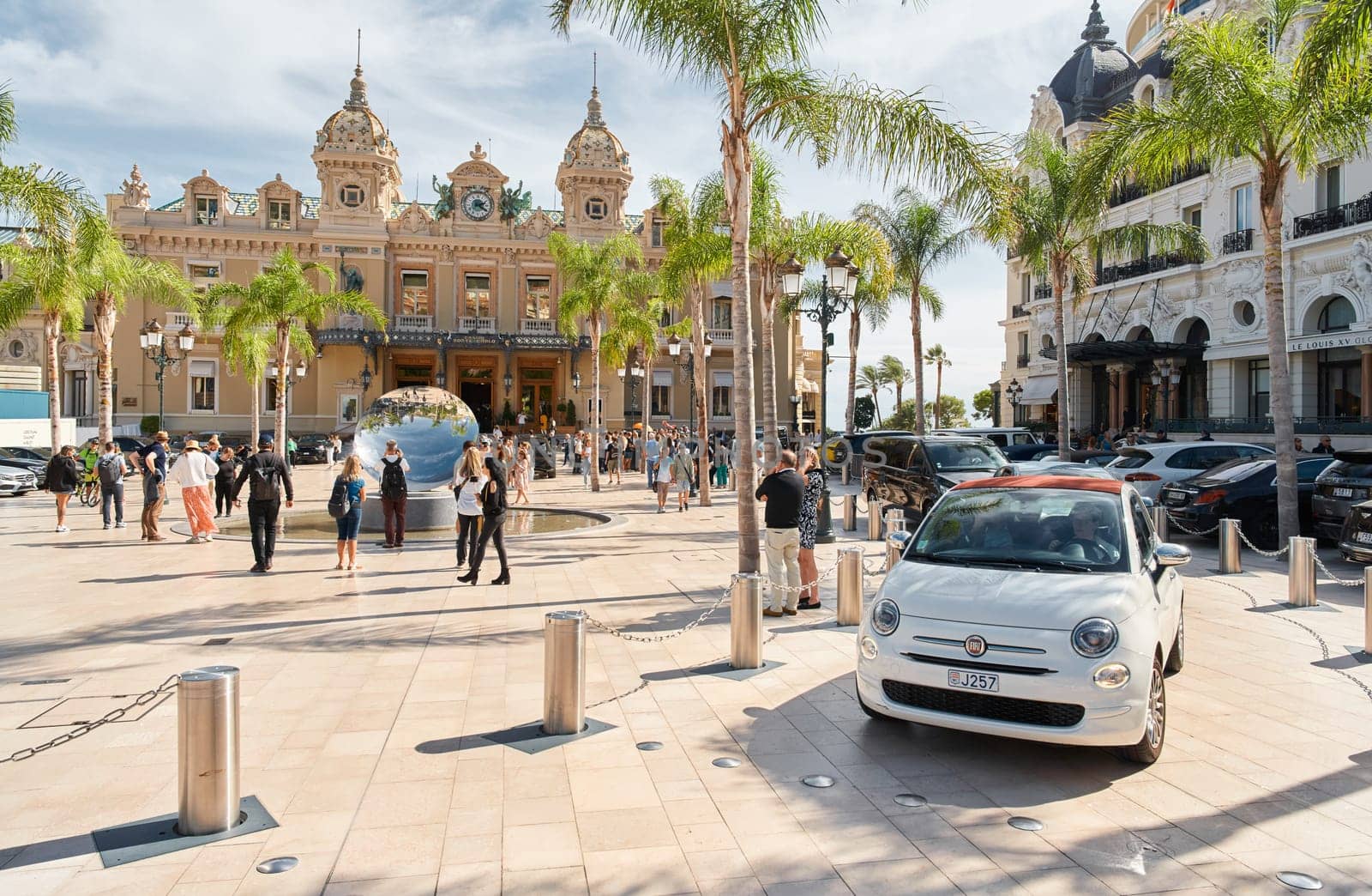 Monaco, Monte-Carlo, 29 September 2022 - Square Casino Monte-Carlo at sunny day, luxury cars, famous Hotel de Paris, wealth life, tourists take pictures of the landmark, pine trees, flowers by vladimirdrozdin