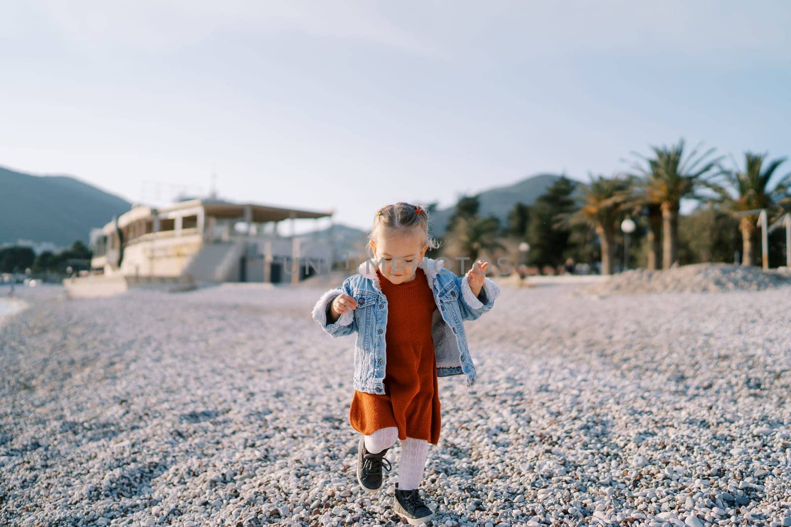 Little smiling girl walks along a pebble beach looking at her feet. High quality photo