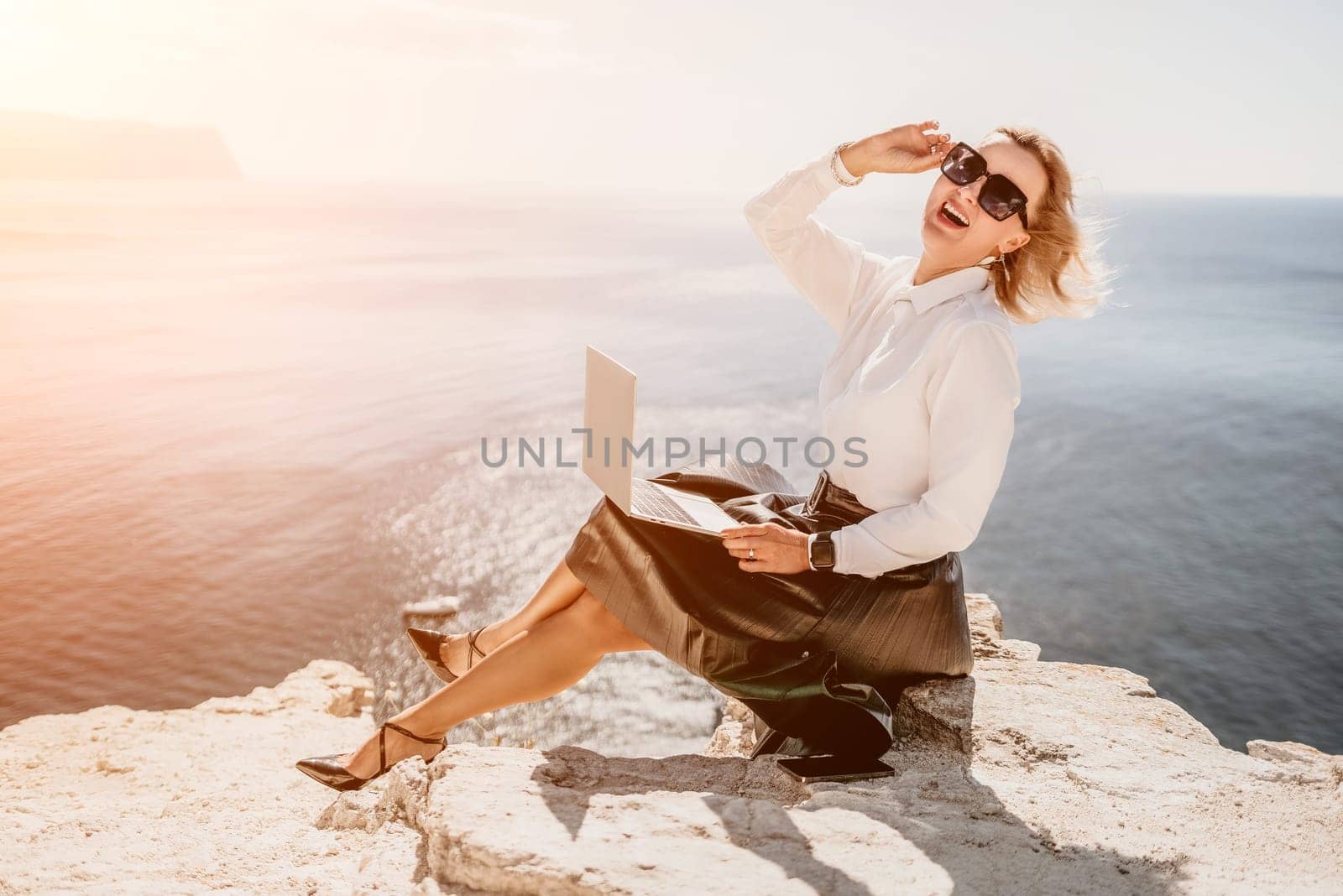 Digital nomad, Business woman working on laptop by the sea. Pretty lady typing on computer by the sea at sunset, makes a business transaction online from a distance. Freelance, remote work on vacation by panophotograph