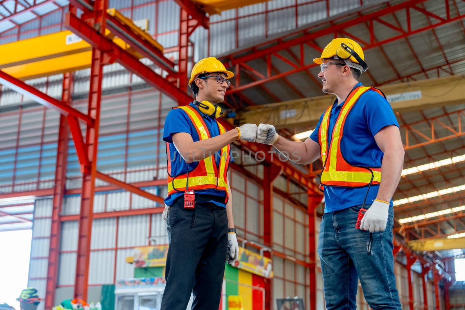 Side view of Caucasian technician workers do hands bump and look happy in factory workplace area.