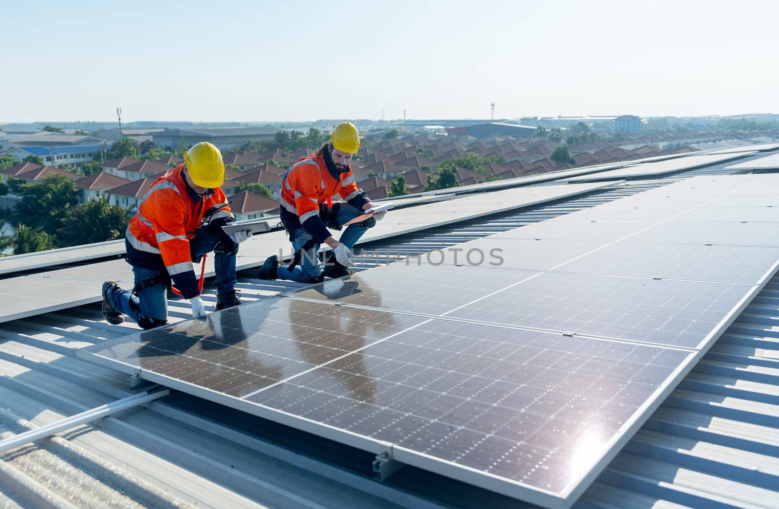 Side view of two Caucasian technician workers check and maintenance the solar cell panels on rooftop of the building or factory.