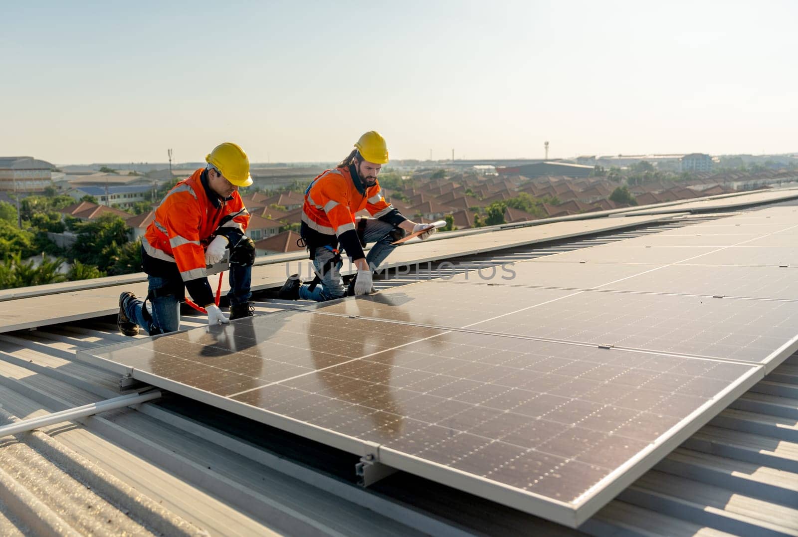 Technician workers hold document pad and tablet check and maintenance the solar panels on rooftop of the building or factory.