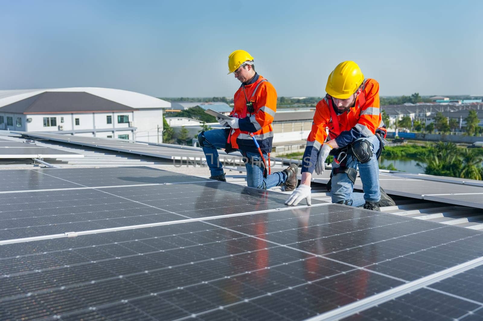 Side view of two Caucasian workers hold document pad and tablet check and maintenance the solar cell panels on rooftop of the building or factory.