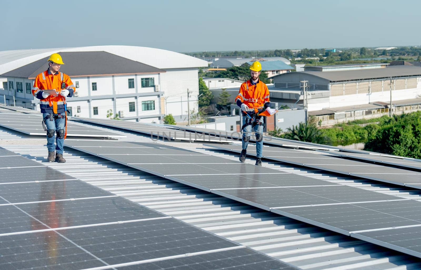 Two technician of industrial worker walk and discuss on rooftop of the factory building about maintenance of solar cell panels with green and sustainable energy for good environment.