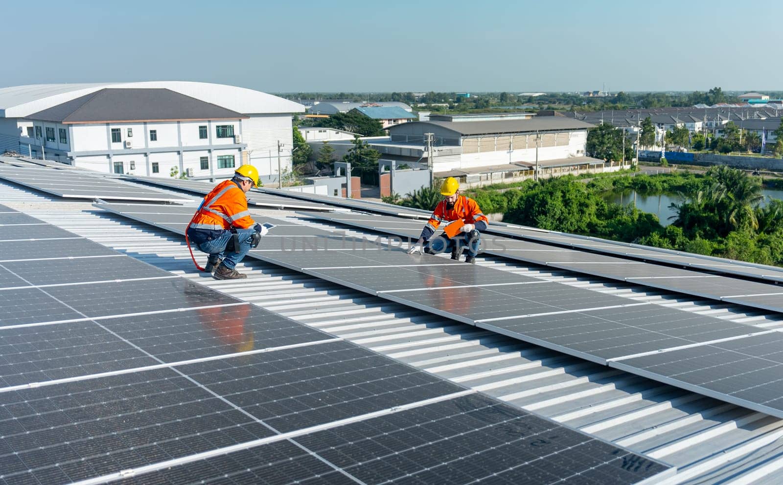 Wide shot two Caucasian technician workers sit on rooftop and discuss abot maintenance the solar cell panels on rooftop of factory or the building. Green and sustainable energy concept.