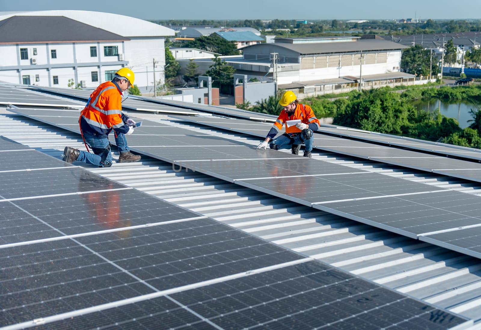 Two Caucasian technician workers sit on rooftop area to check and maintenance the solar cell panels on rooftop of factory or the building. Green and sustainable energy concept.