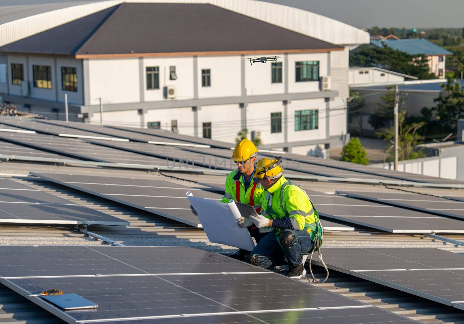 Side view of two Caucasian technician workers use construction plan and tablet to check and maintenance solar cell panels on rooftop of factory or the building. Green and sustainable energy concept.