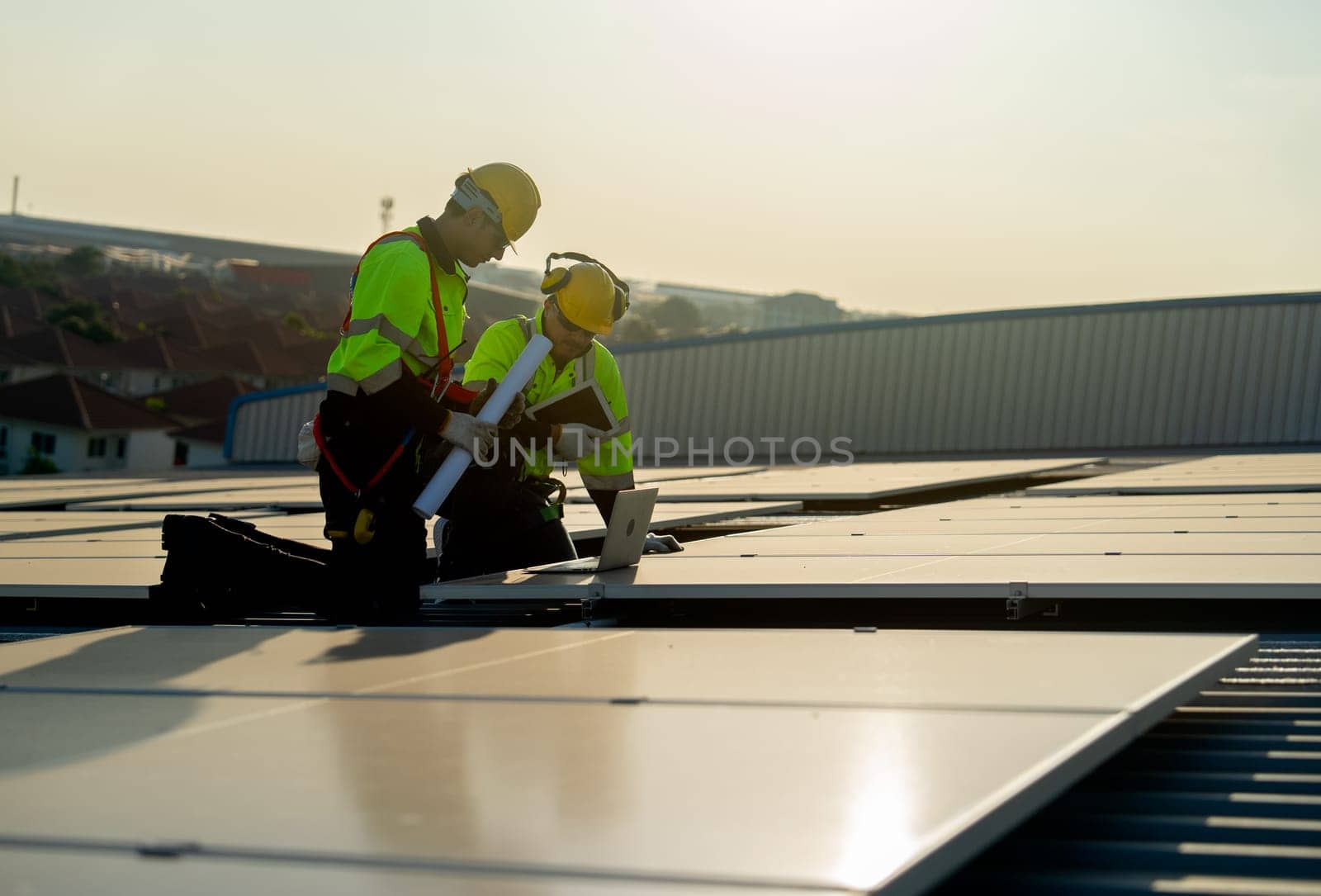 Side view of two Caucasian technician workers look at laptop to check and maintenance solar cell panels on rooftop of factory or the building. Green and sustainable energy concept.