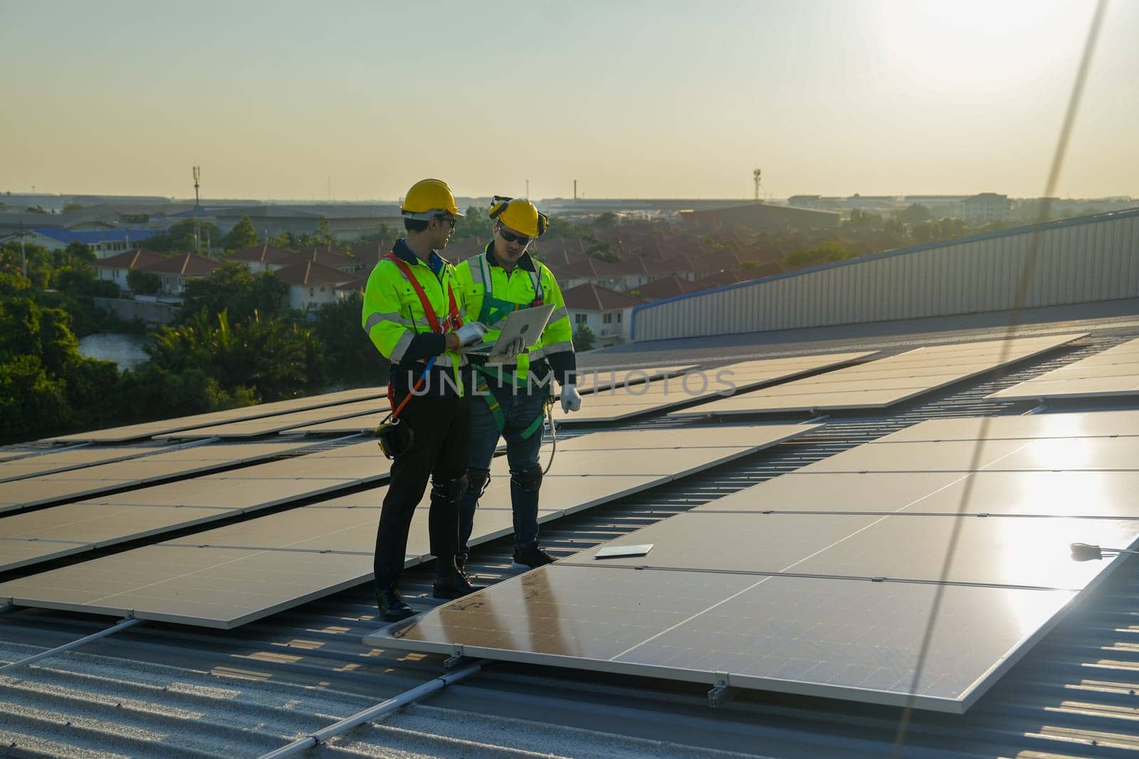Two Caucasian technician workers stand on rooftop and discuss about the maintenance solar cell panels on rooftop of factory or the building. Green and sustainable energy concept.