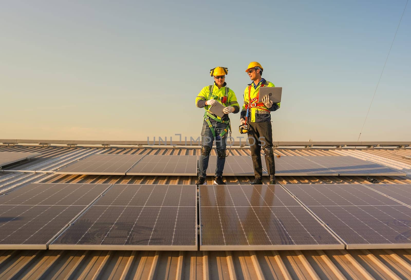 Front view of two Caucasian technician workers stand on rooftop and discuss about the maintenance solar cell panels on rooftop of factory or the building. Green and sustainable energy concept.