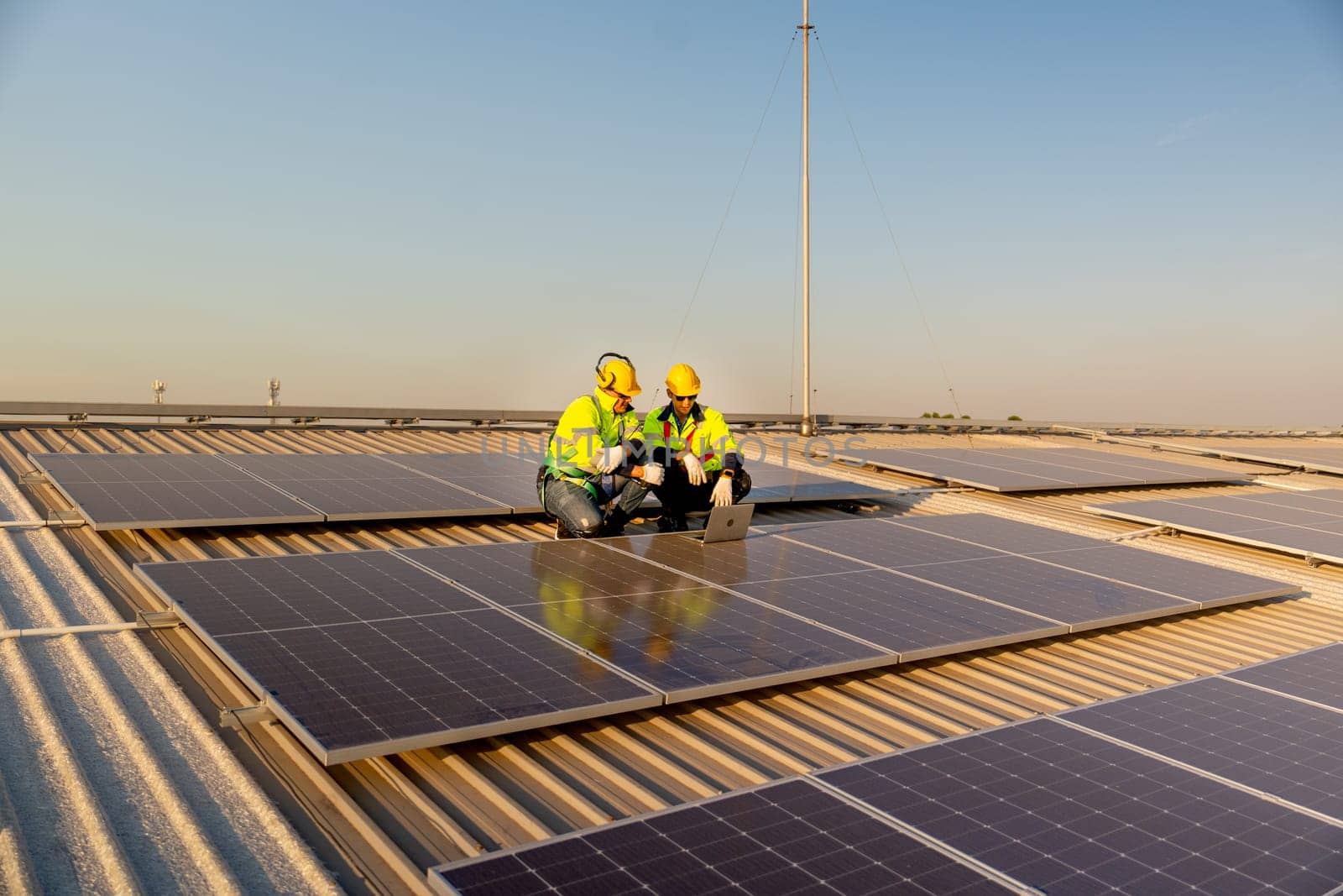 Wide shot two Caucasian technician workers sit on rooftop and discuss about the maintenance solar cell panels on rooftop of factory or the building. Green and sustainable energy concept.