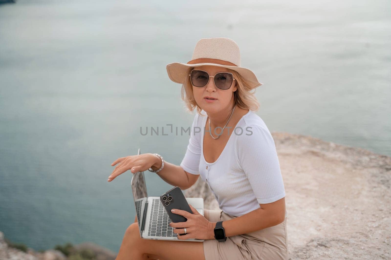 Freelance women sea working on the computer. Good looking middle aged woman typing on a laptop keyboard outdoors with a beautiful sea view. The concept of remote work. by Matiunina