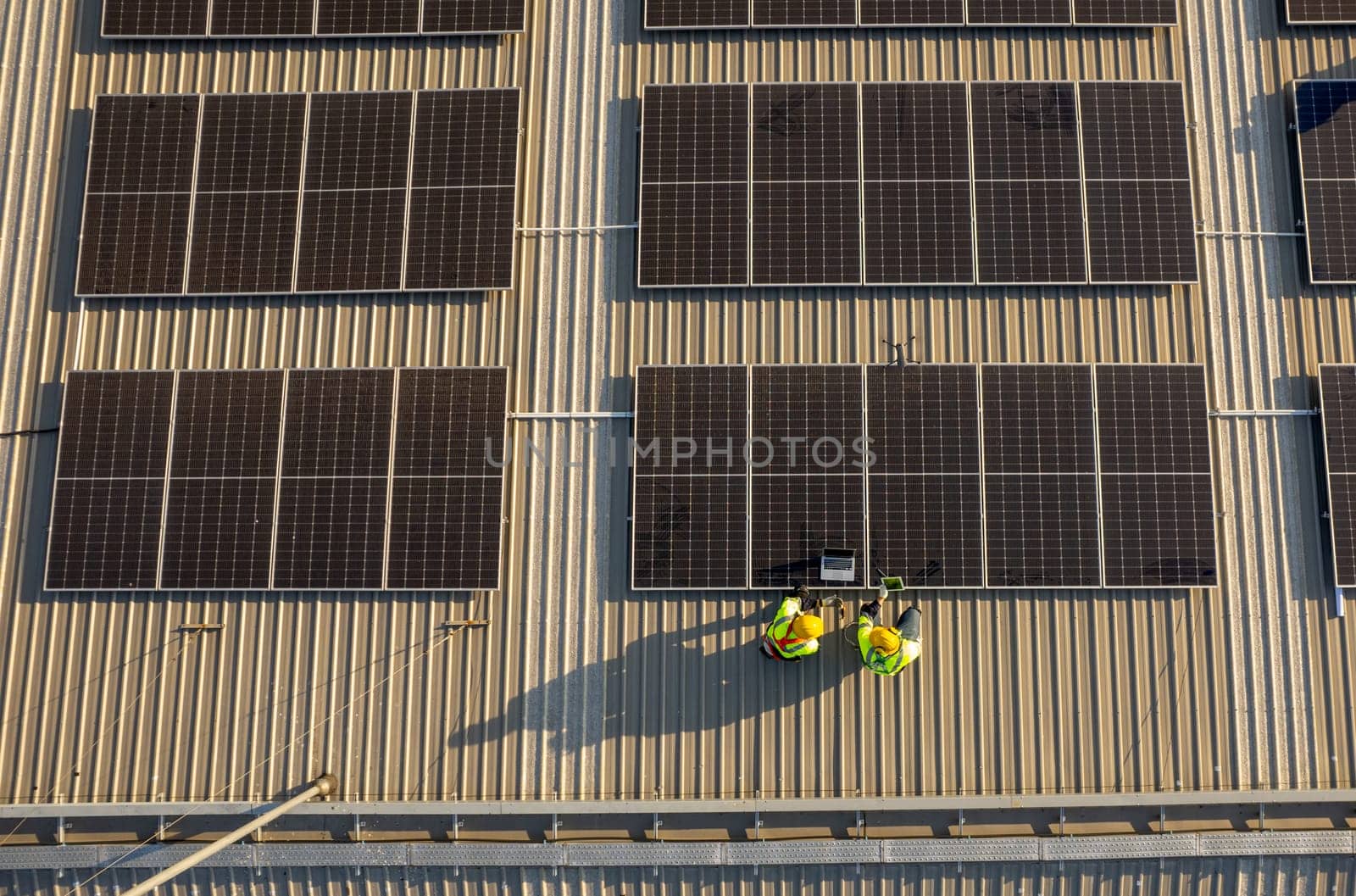 Top view or drone view of two technician workers use laptop and tablet to check and maintenance solar cell panels on rooftop of factory building with green and sustainable energy concept.