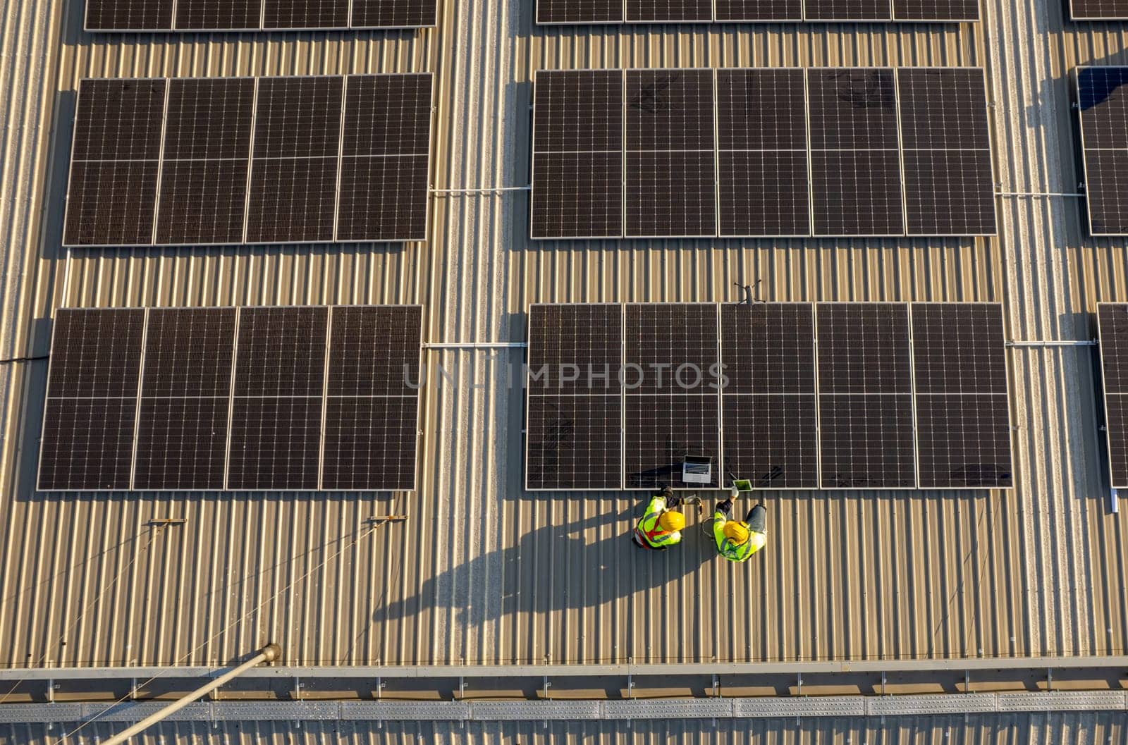 Top view or drone view of two technician workers use laptop and tablet to check and maintenance solar cell panels on rooftop of factory building with green and sustainable energy concept.