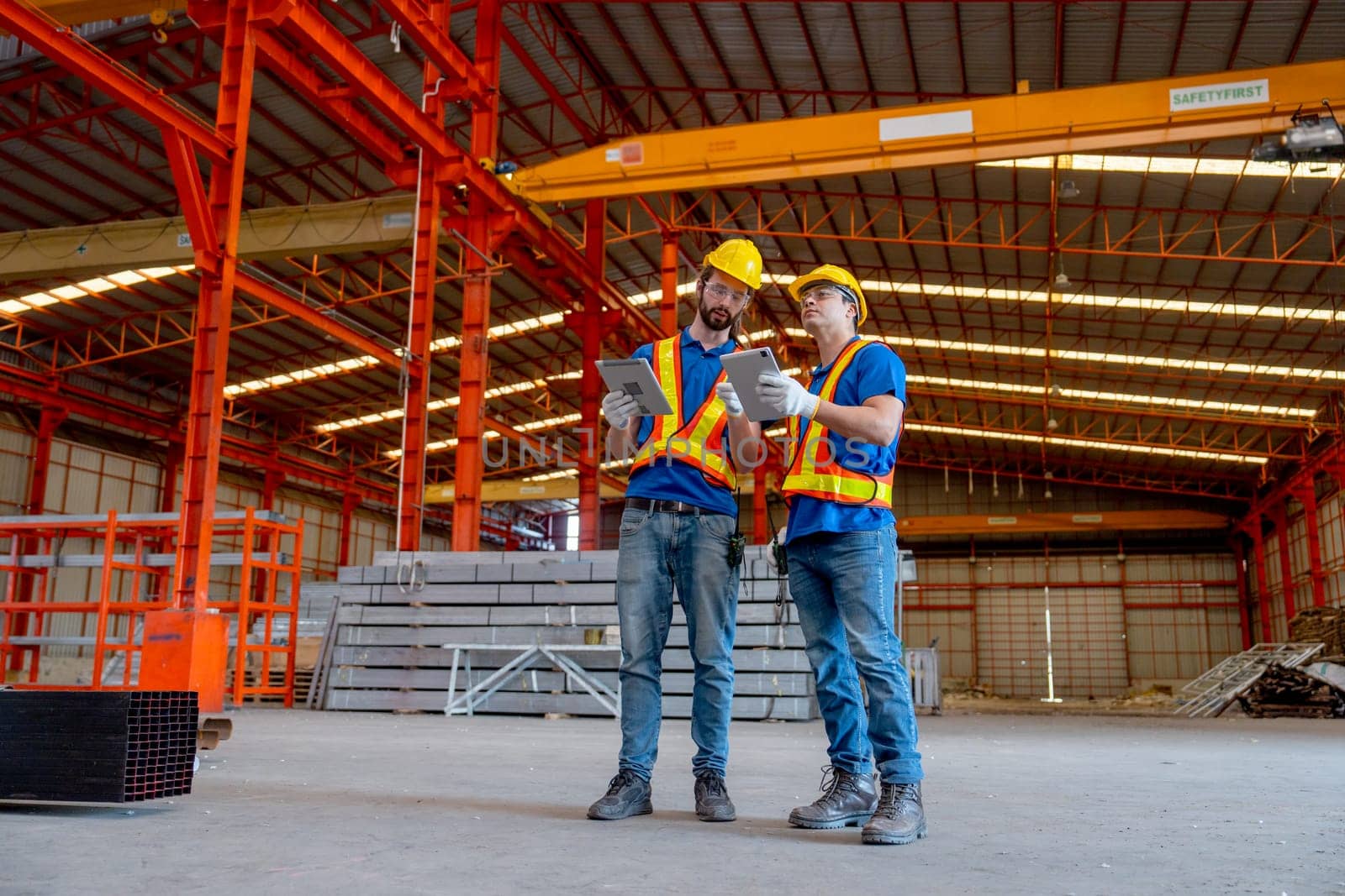 Two Caucasian technician workers hold tablet and stand together to discuss about work in factory workplace area.