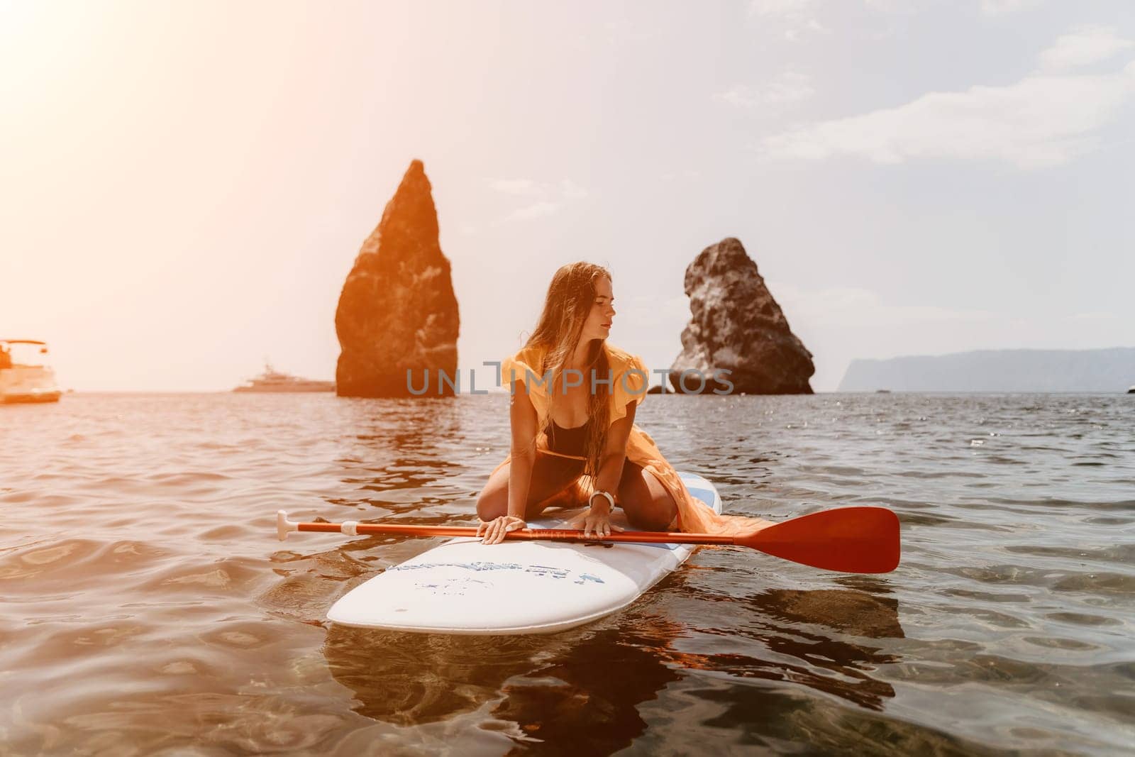 Close up shot of beautiful young caucasian woman with black hair and freckles looking at camera and smiling. Cute woman portrait in a pink bikini posing on a volcanic rock high above the sea