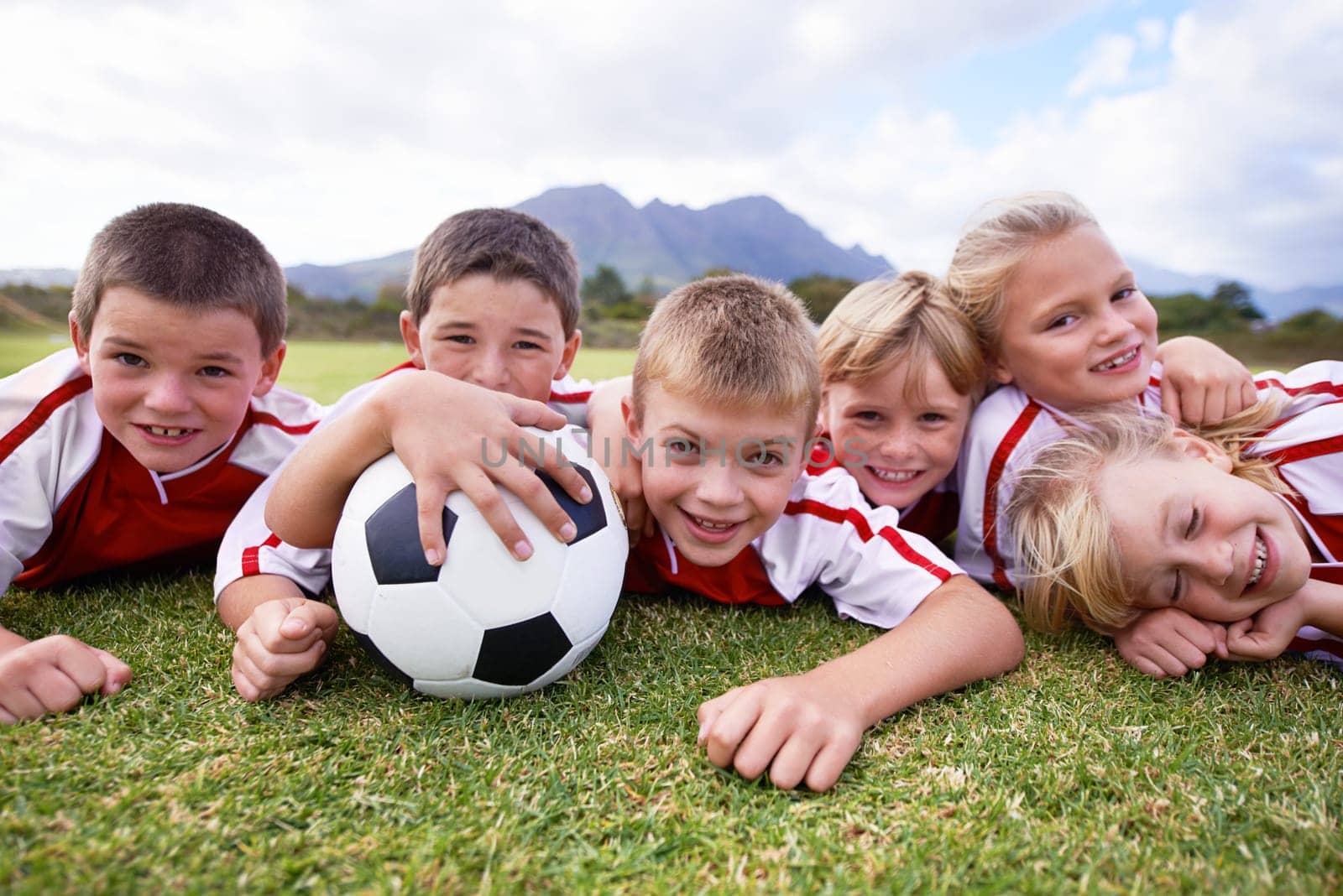 Children, soccer ball and relax on green grass or field for outdoor match, game. or team sports. Group of kids, friends or football players smile lying together for competition on stadium in nature by YuriArcurs