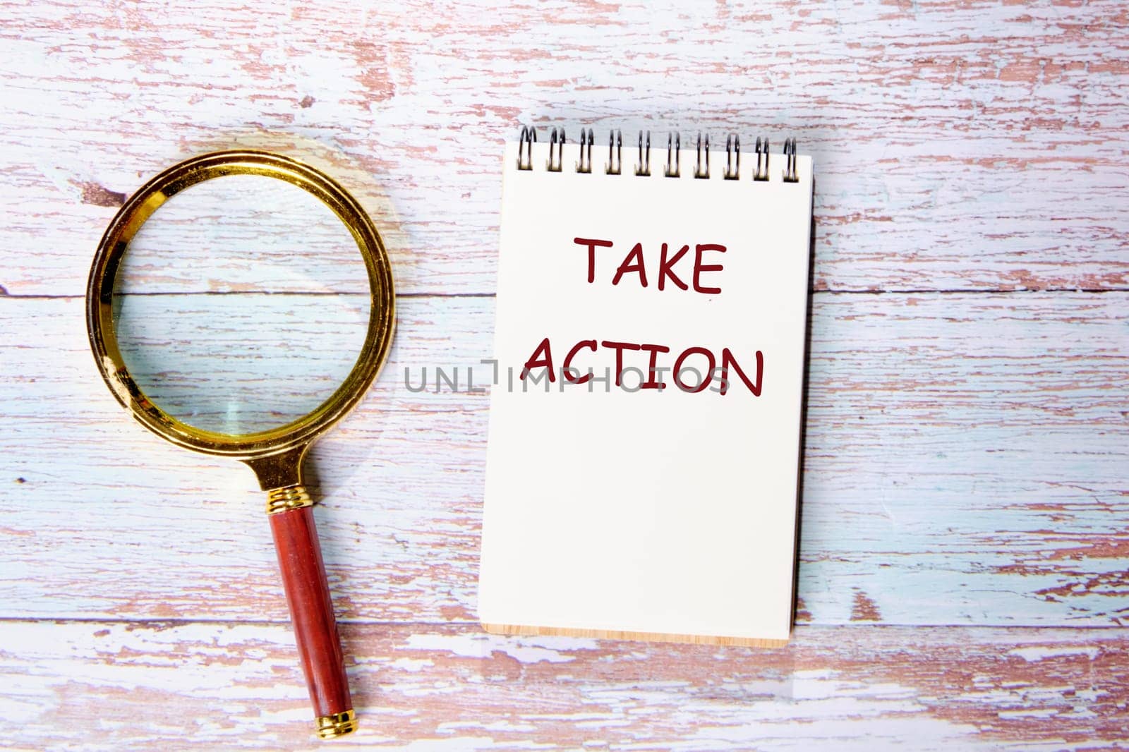 Take Action text written on a notebook on wooden boards next to a magnifying glass