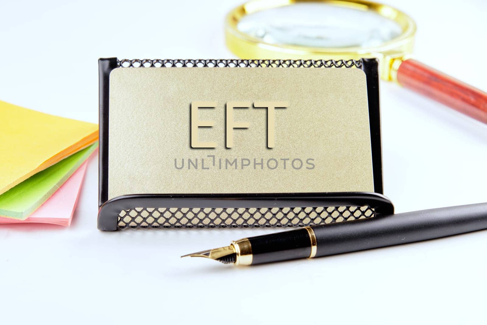 EFT text on a gold plastic card with convex text next to office supplies on a white background