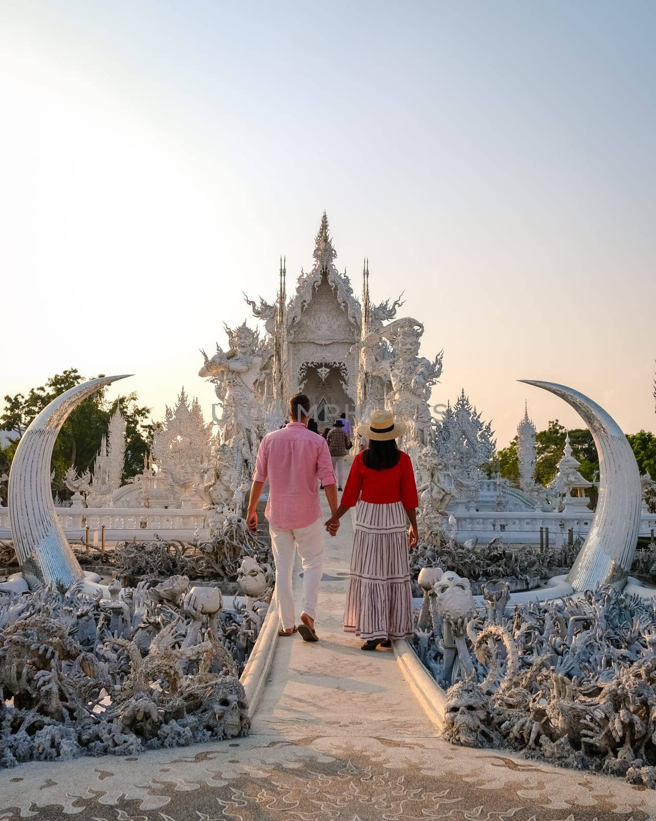 White Temple Chiang Rai Thailand,a diverse couple of men and women visit Wat Rong Khun temple at sunset, Northern Thailand.