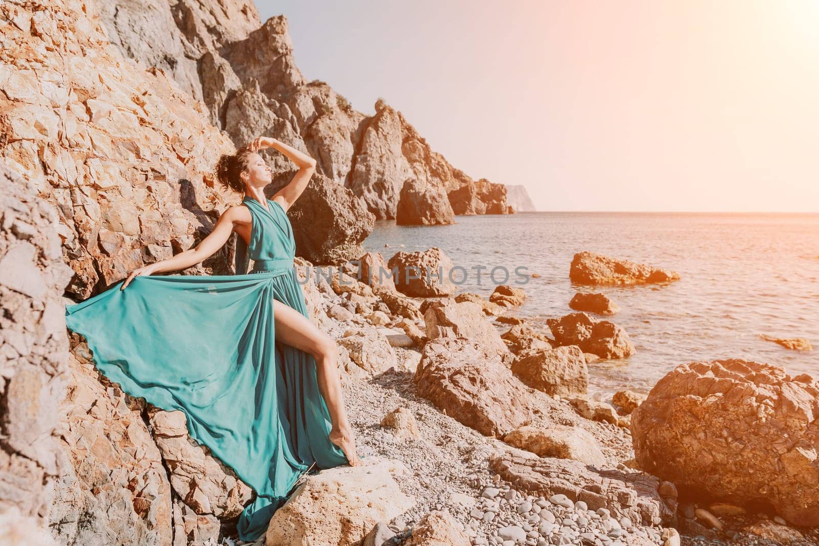 Side view a Young beautiful sensual woman with black hair in a long mint dress posing on a beach with calm sea bokeh lights on sunny day. Girl on the nature on blue sky background. Fashion photo by panophotograph