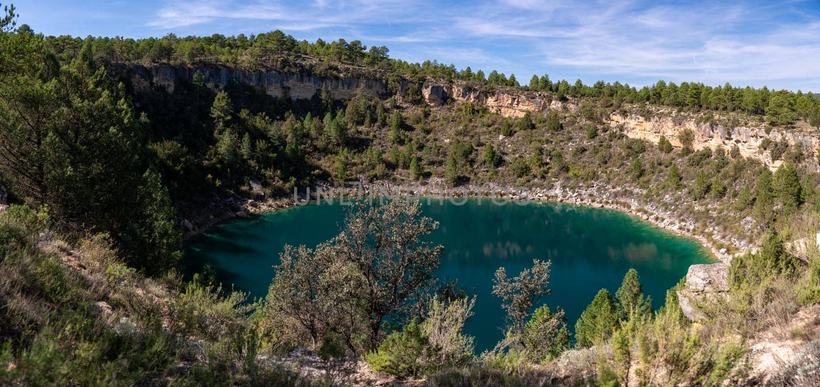 A tranquil turquoise lake within a lush forest under a clear sky.