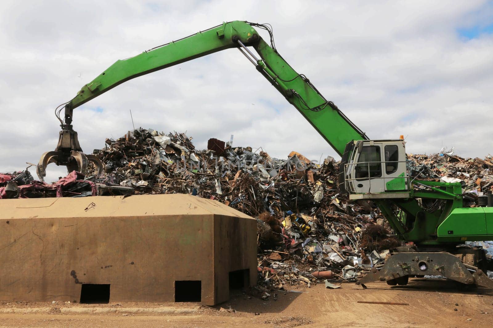 A crane with jaws loads scrap metal for recycling. Ecological concept, metal recycling. Crane against the sky.