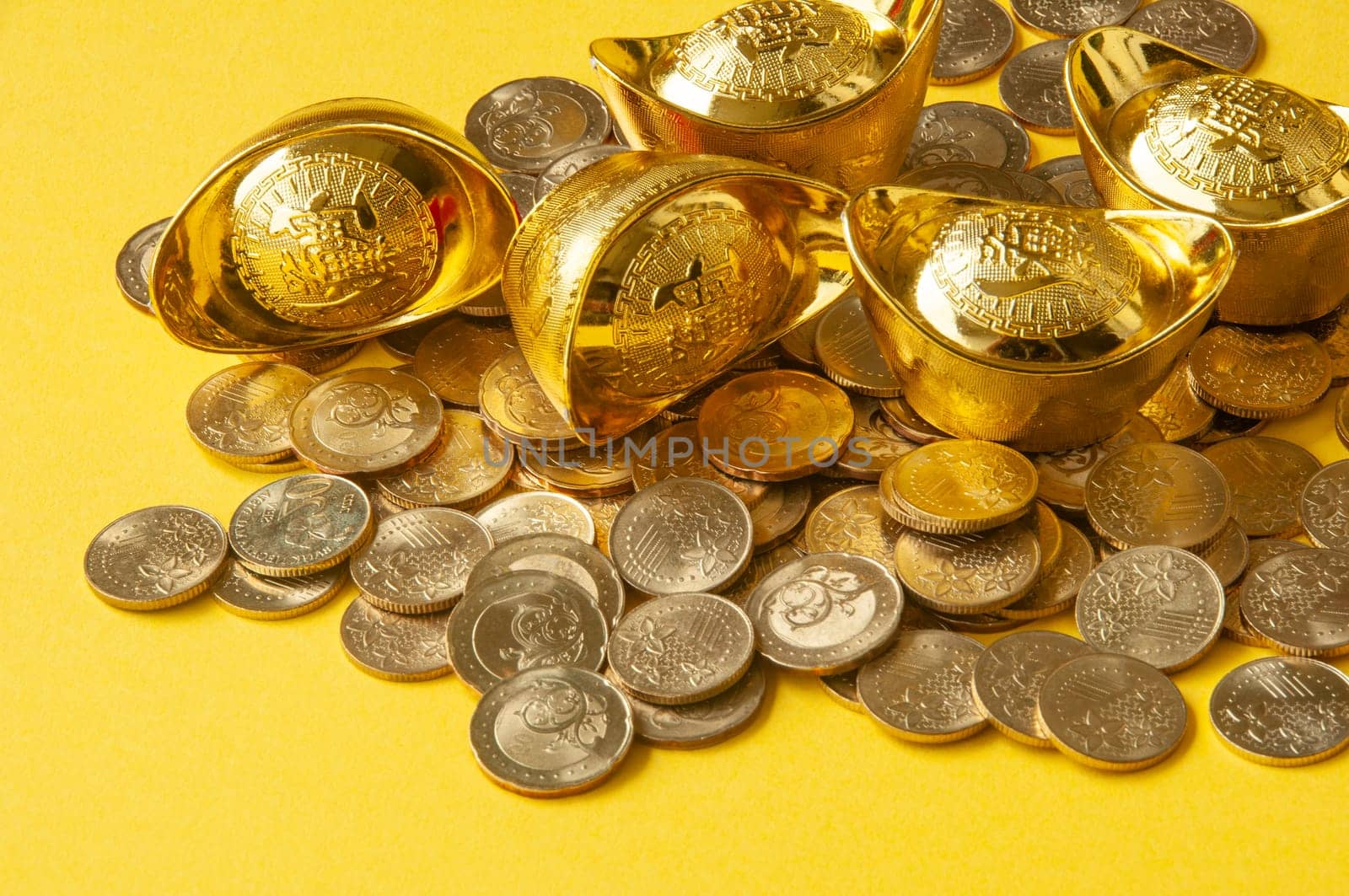 Close up view of golden ingot and coins with yellow cover background.