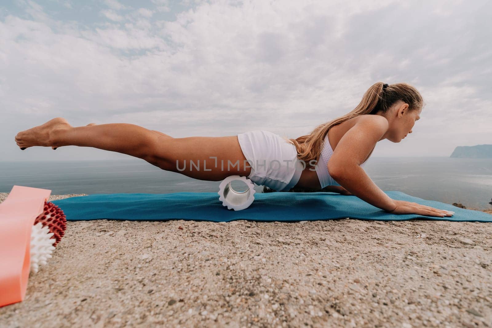 Woman sea pilates. Sporty, middle-aged woman practicing pilates in park near the sea. trains on a yoga mat and exudes a happy and active demeanor, promoting the idea of a healthy lifestyle through exercise and meditation.