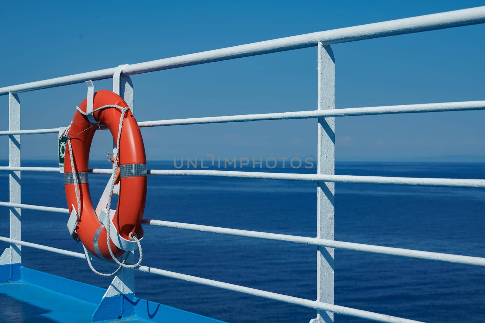 a red lifebuoy hangs on board a ferry cruise ship against the backdrop of a blue sea and a cloudless sky by Costin