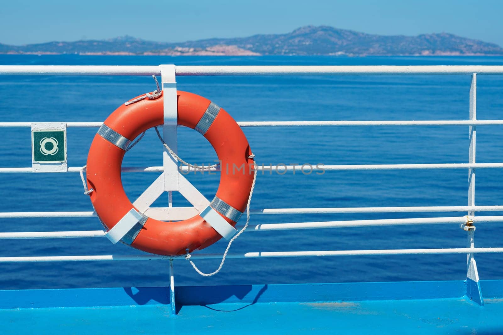 a red lifebuoy hangs on board a ferry cruise ship against the backdrop of a blue sea and a cloudless sky by Costin