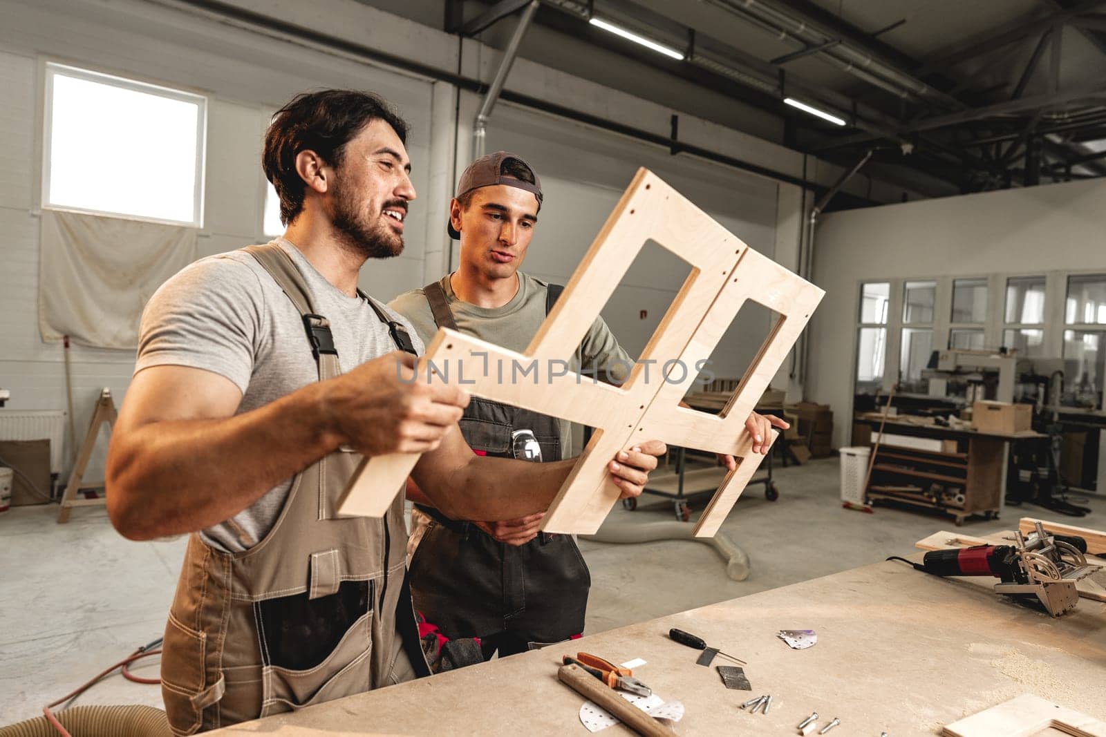 Two young men carpenters making furniture in warehouse of wood factory by Fabrikasimf
