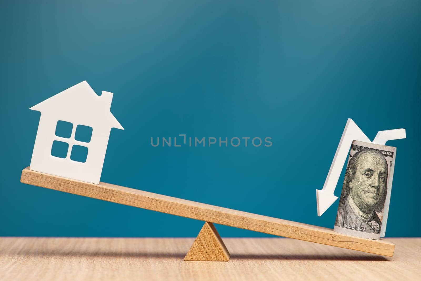 Buying cheap real estate. Banner on the theme of buying a house. One hundred dollar bill with an arrow pointing down and a house model on the scales as a symbol of a good real estate deal. by SERSOL