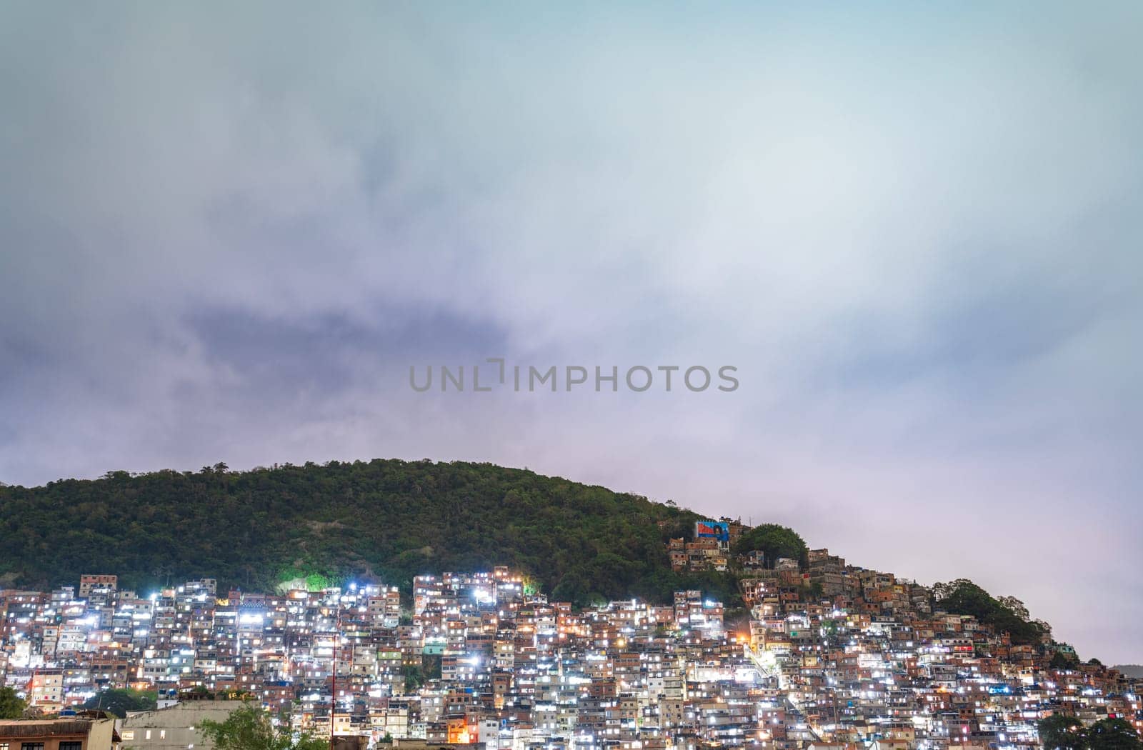 Illuminated Favela at Dusk Against a Moody Sky by FerradalFCG